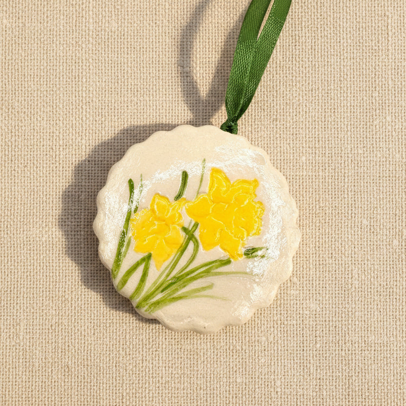 Decorative circular clay ornament with yellow daffodil flowers on a pale beige background
