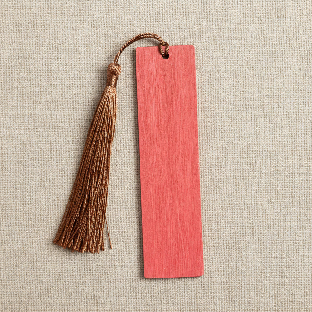 Wooden bookmark with a brown tassel on a linen background (back of bookmark shown, autumnal red/orange colour)