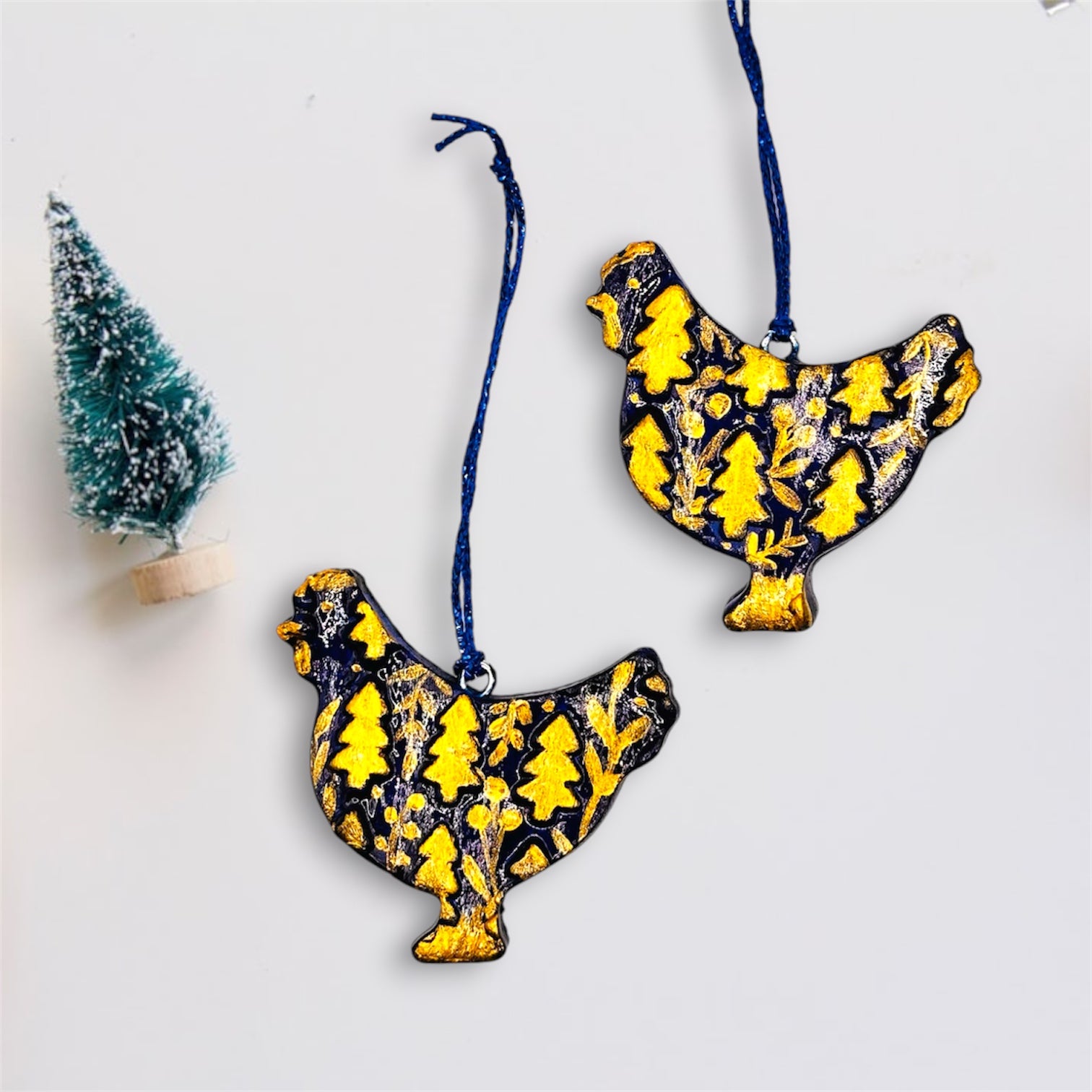 Two dark blue clay chicken ornaments with gold tree patterns on a white background.