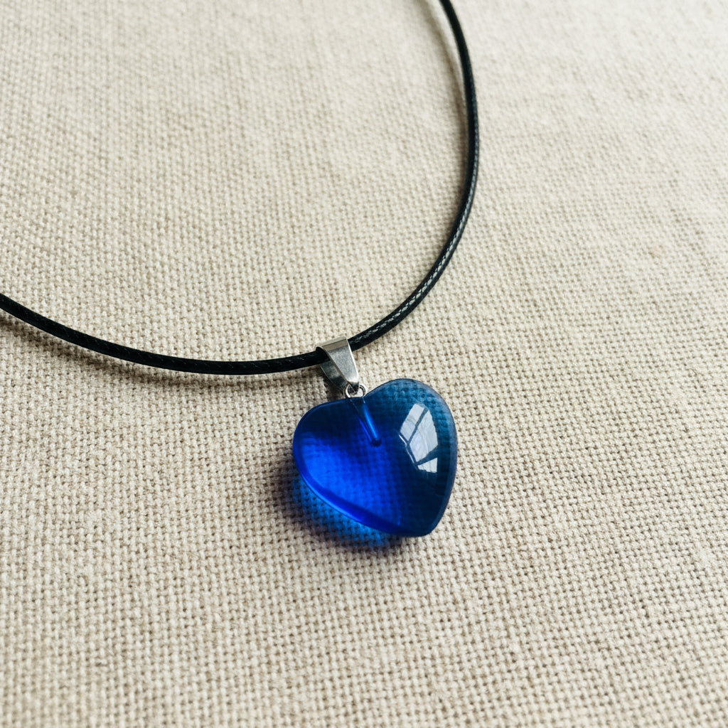 Blue heart-shaped pendant on a black cord against a neutral background