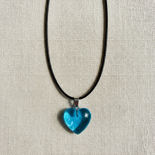 Blue heart-shaped pendant on a black cord against a neutral background