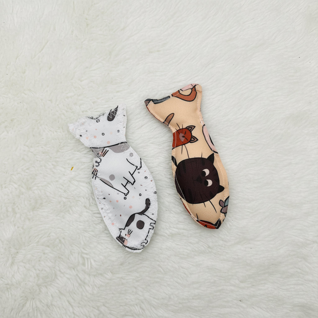 Two fish-shaped fabric cat toys with cat patterns, one in beige and the other in white, displayed on a plain white surface.