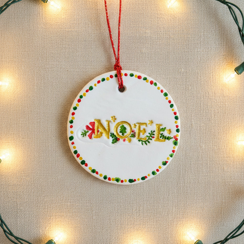 Round ceramic ornament with 'NOEL' text and festive design on a light background