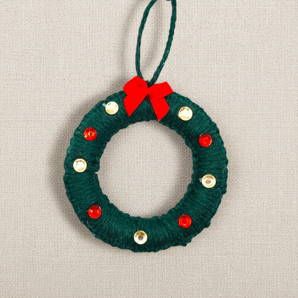 Green yarn wreath ornament with red bow and gold and red gems on a light background