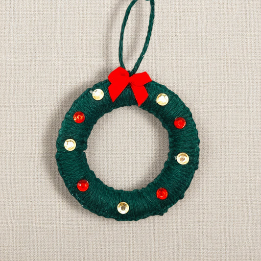 Green yarn wreath ornament with red bow and gold and red gems on a light background