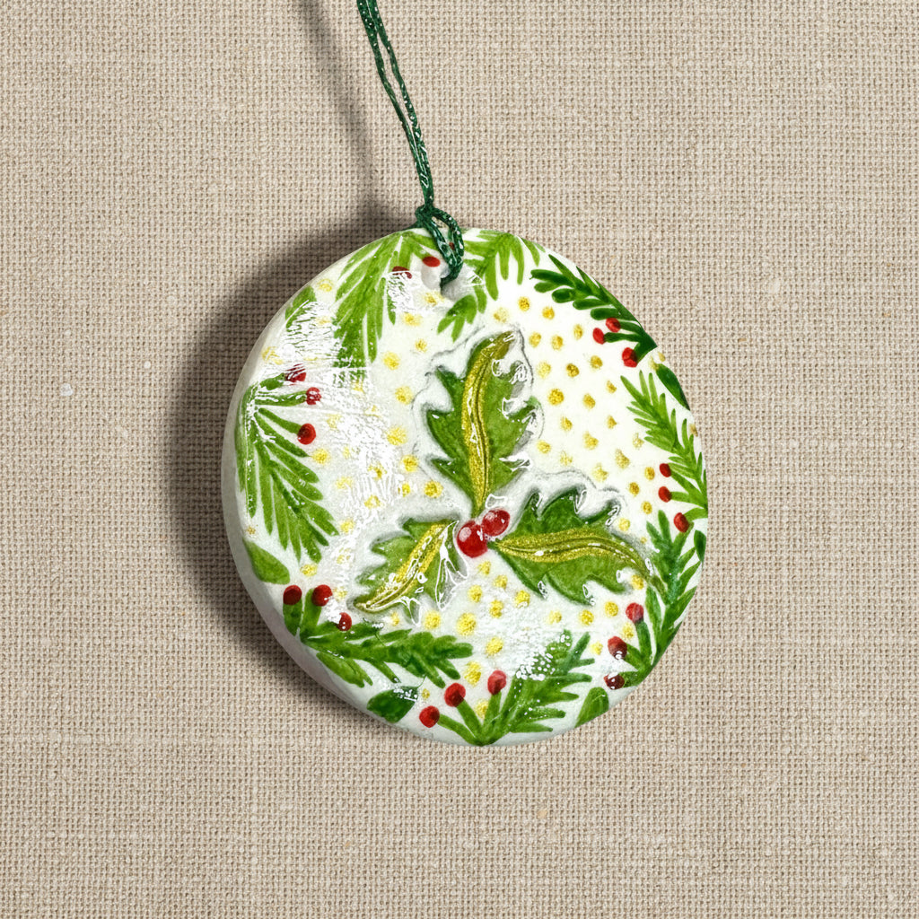 Decorative Christmas ornament with green holly leaves and red berries on a light background