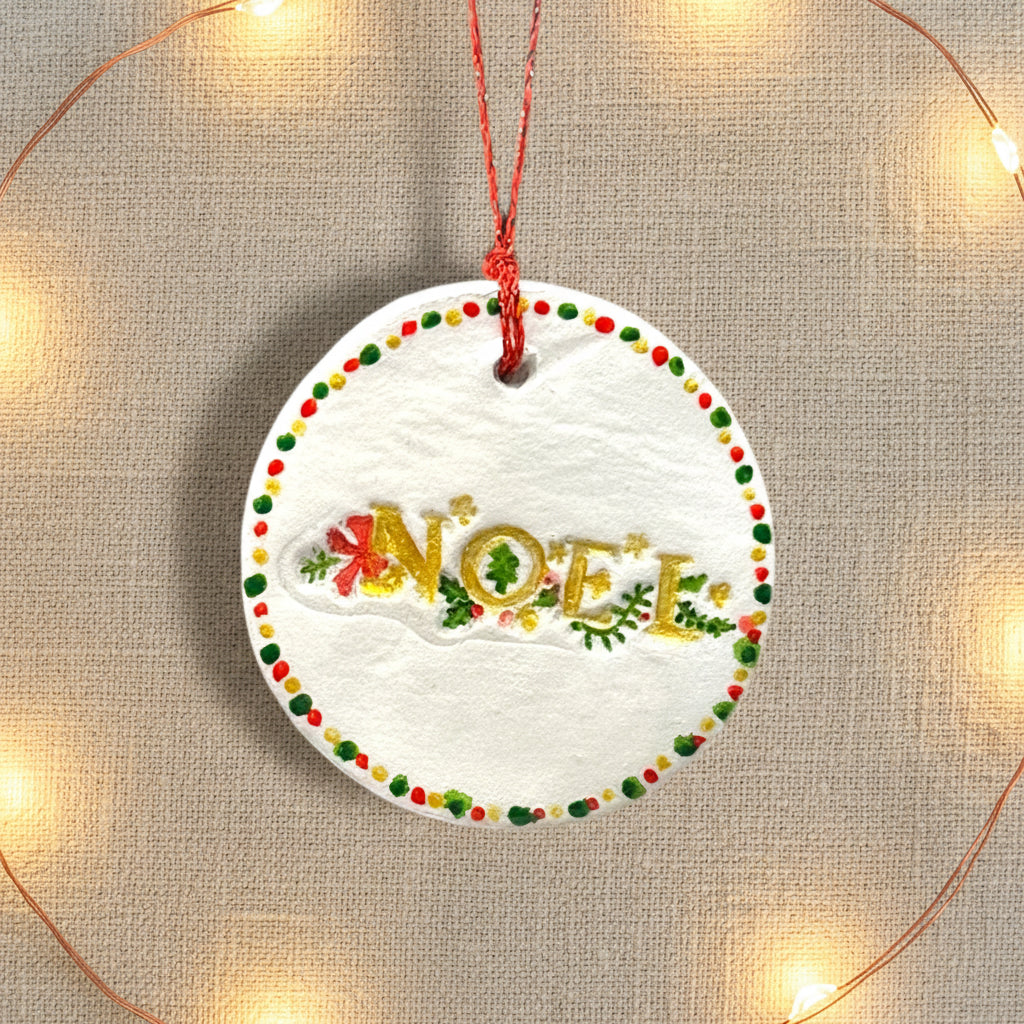 Round white ornament with 'NOEL' text and colorful border on a light background