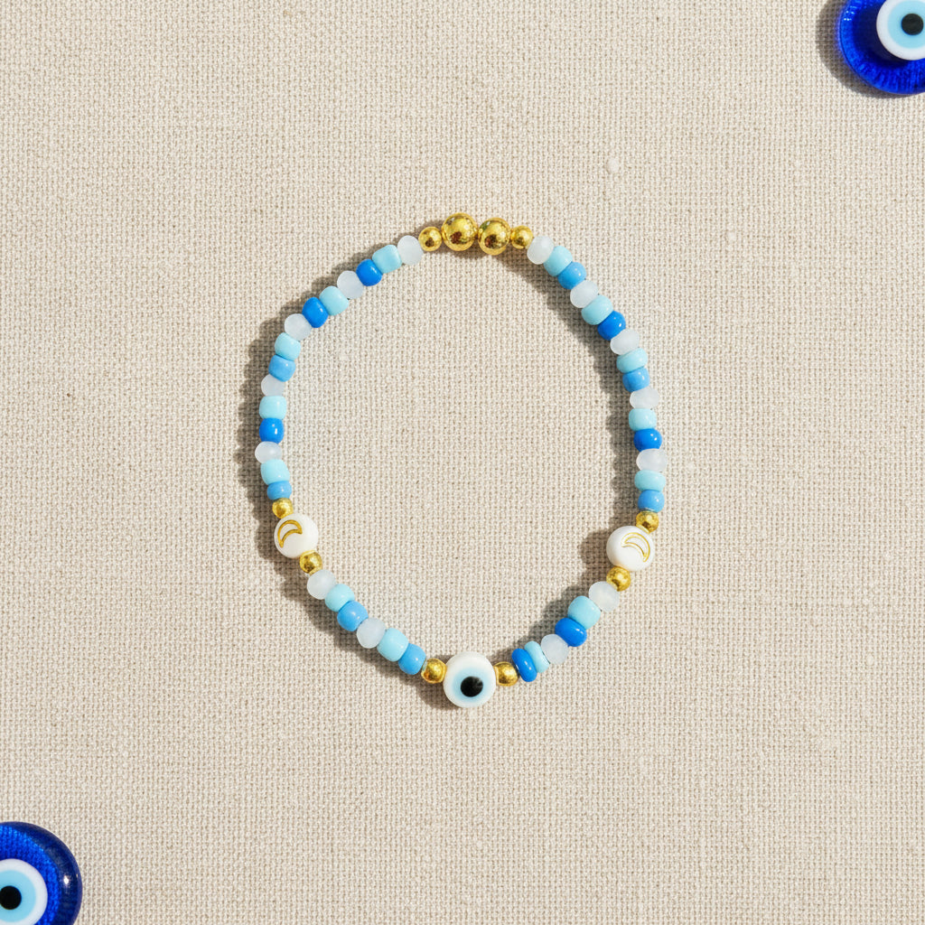 Colourful blue and white beaded bracelet with gold accents and evil eye bead on a linen background
