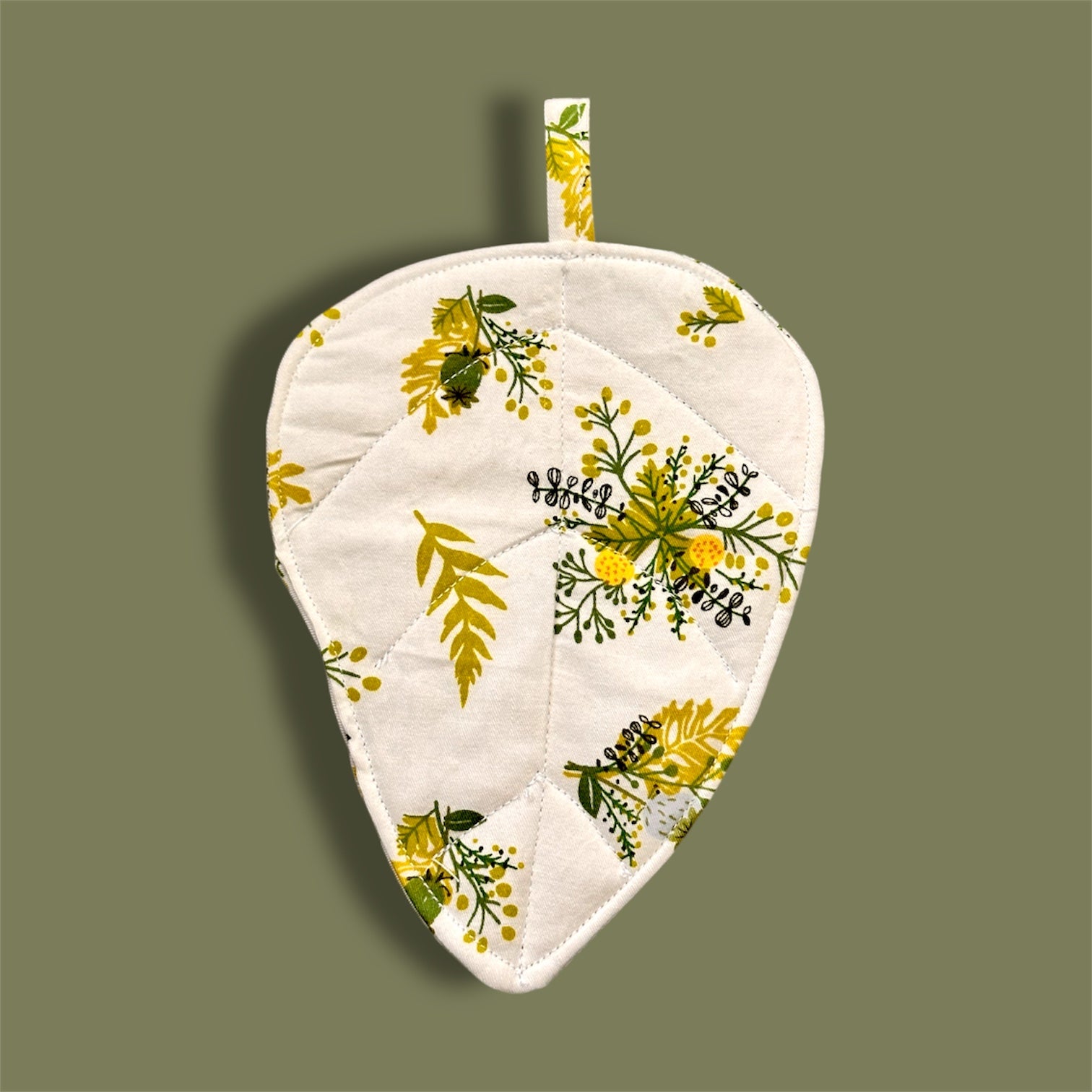 Floral-patterned leaf shaped fabric coaster on a green background