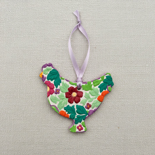 Decorative ornament shaped like a chicken with floral patterns on a plain background with light purple ribbon to hang