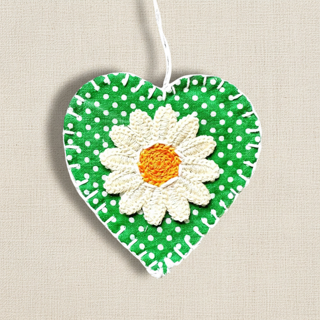 Heart-shaped green fabric ornament with a white daisy flower design on a neutral background