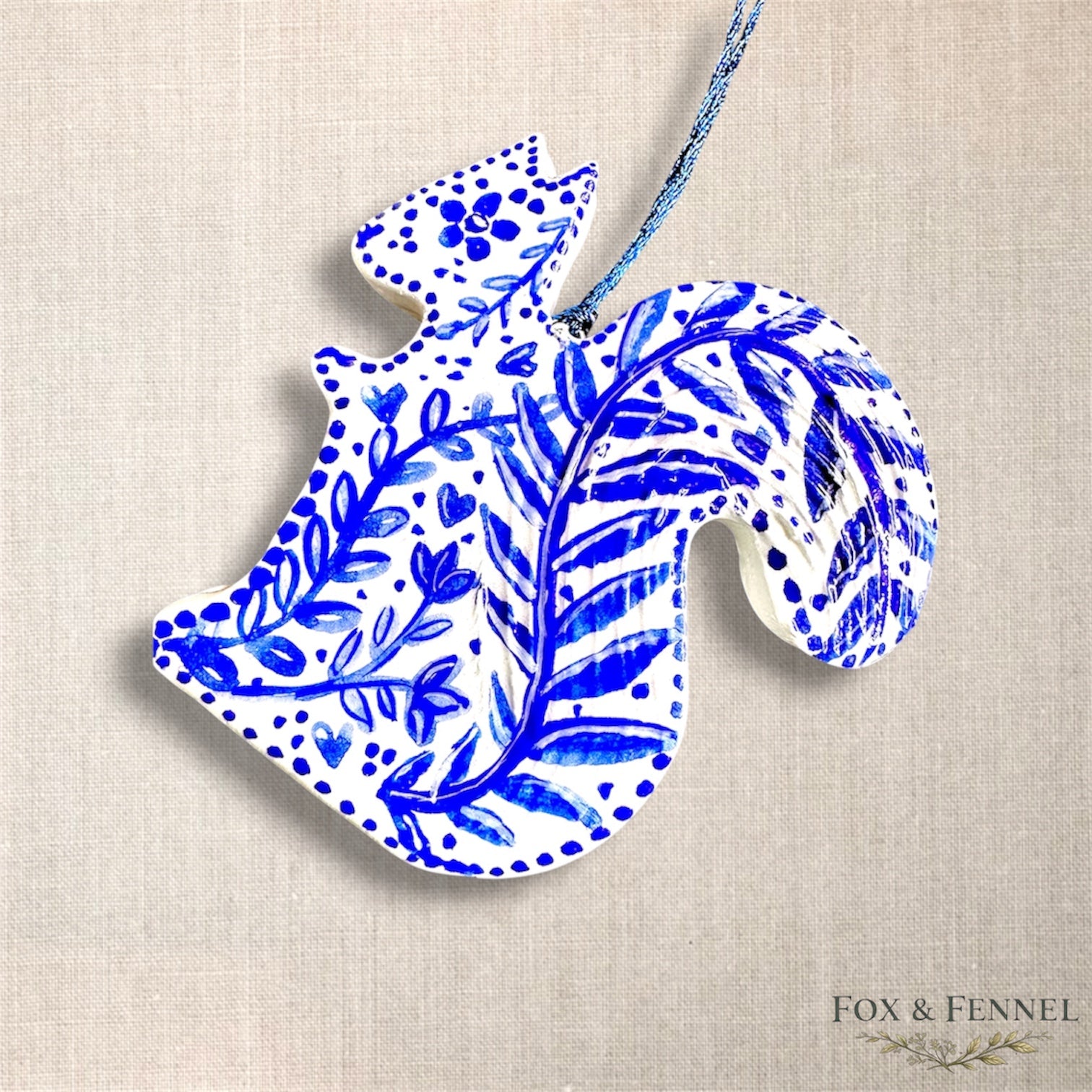 Decorative off white, clay squirrel hanging decoration with hand painted blue leaves and flowers. Blue string to hang