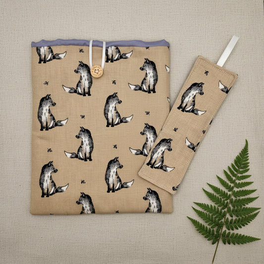 A handmade, fabric fox themed kindle cover with matching fabric bookmark.
Fabric for cover is natural colour with monochrome foxes, lilac lining, and elastic loop and button, bookmark has white ribbon at the top.