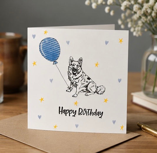 Birthday card with a German shepherd dog and balloon illustration on a wooden surface.
