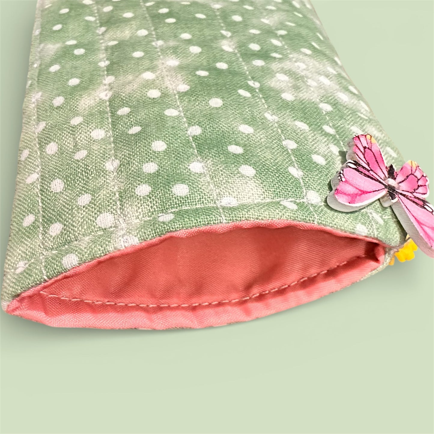 Green and white polka dot soft fabric glasses pouch with pink/coral interior, featuring a decorative butterfly button on a light green background.