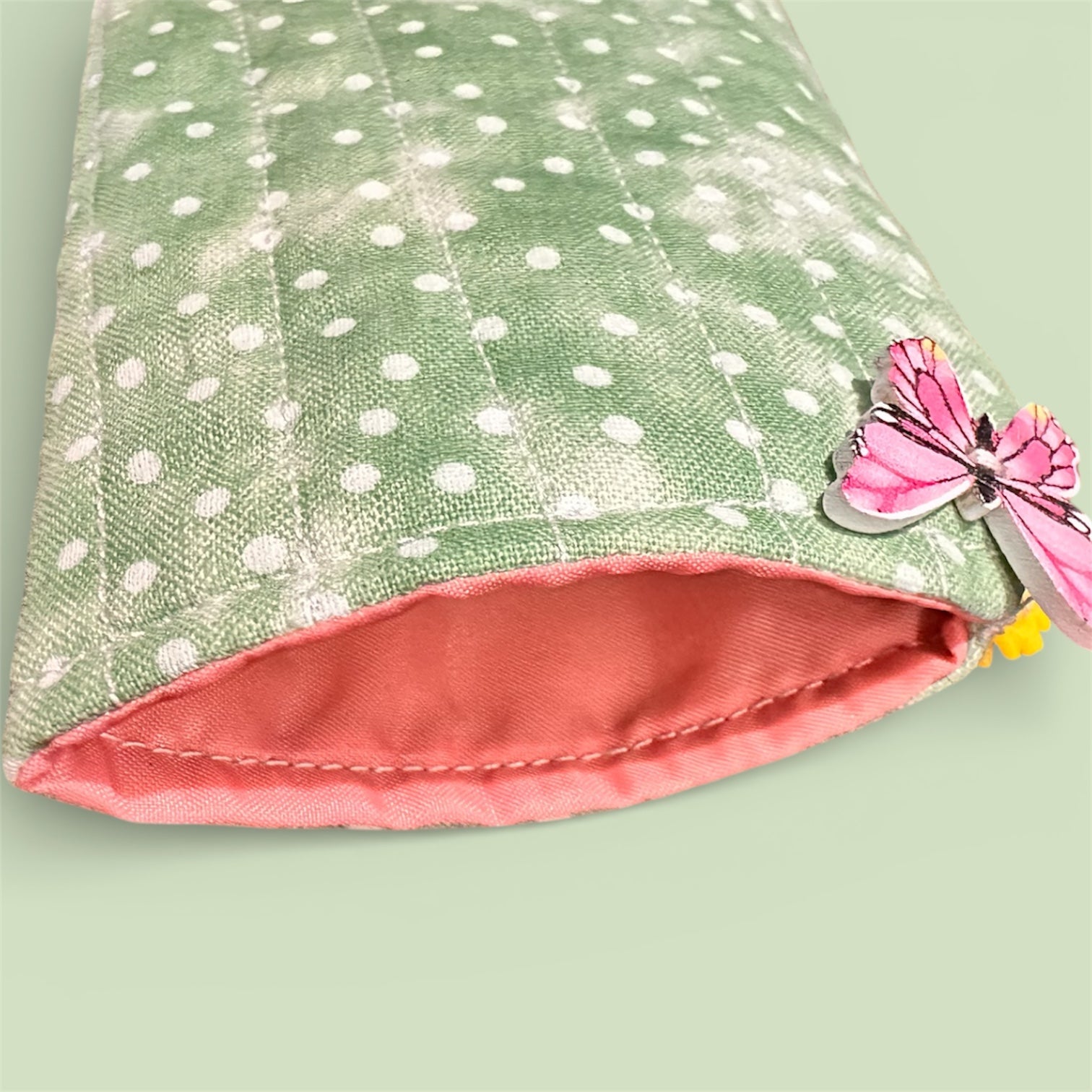 Green and white polka dot soft fabric glasses pouch with pink/coral interior, featuring a decorative butterfly button on a light green background.