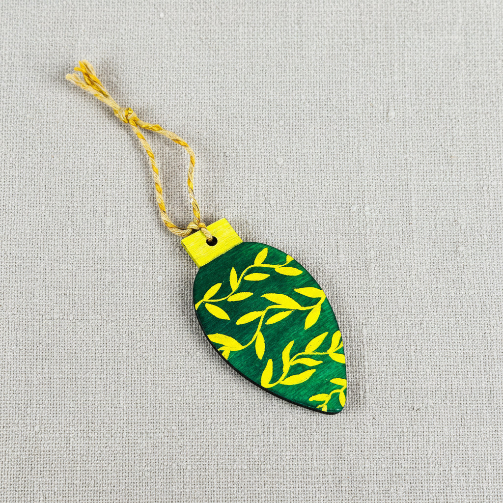 Green leaf-shaped ornament with gold hand painted leaves and twine to hang on a neutral background