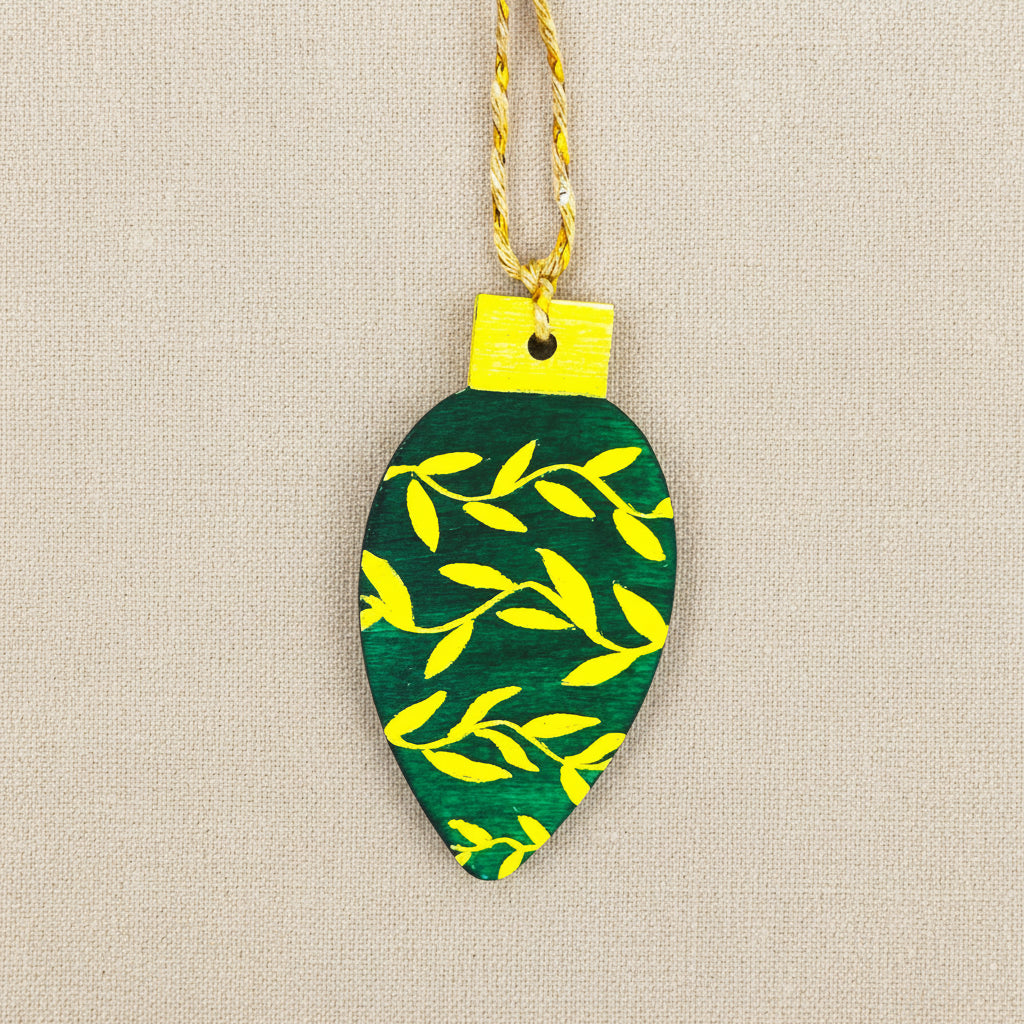 Decorative ornament shaped like a green leaf with gold leaf patterns on a neutral background