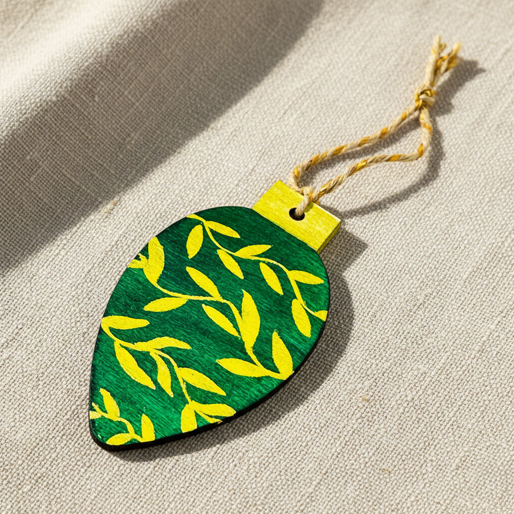 Green and gold leaf-shaped ornament with a string on a neutral background