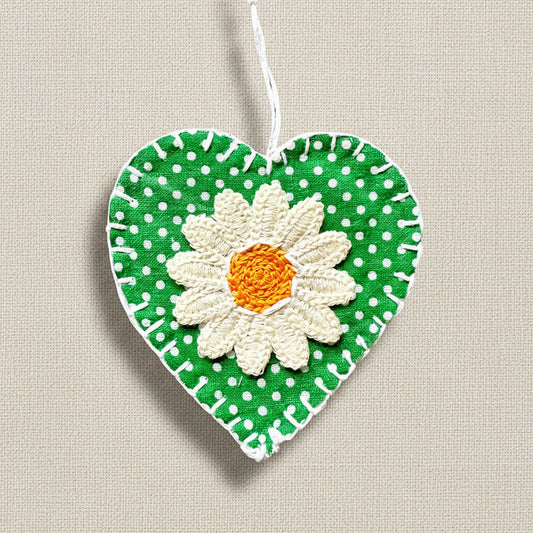 A hand-stitched heart-shaped decoration featuring a green and white polka dot background with a central daisy motif.