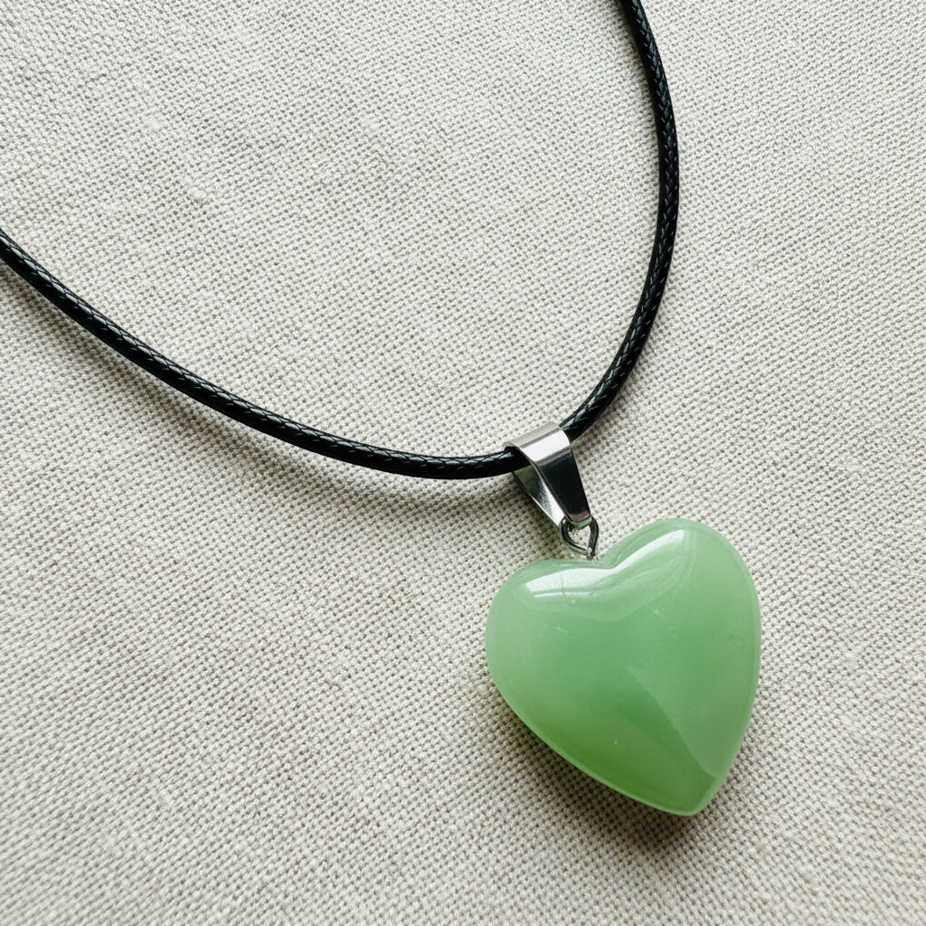 Heart-shaped green pendant on a black cord against a neutral background