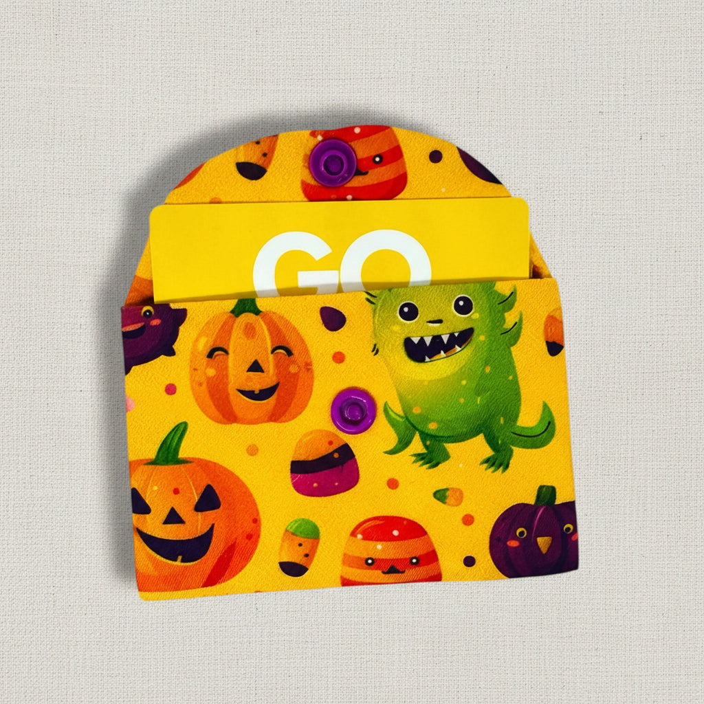 Yellow card wallet with Halloween-themed design featuring pumpkins, a monster, and candy on a white background.