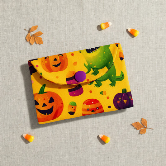 Colourful Halloween-themed card wallet with pumpkins, ghosts, and candy corn on a yellow background.