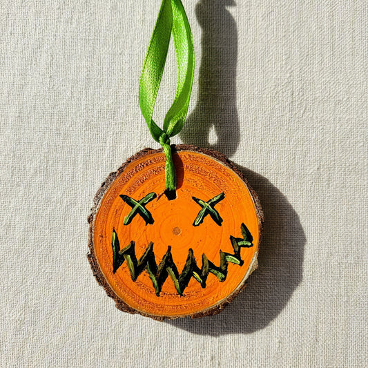 Hand painted wood slice with Halloween pumpkin details and green ribbon to hang