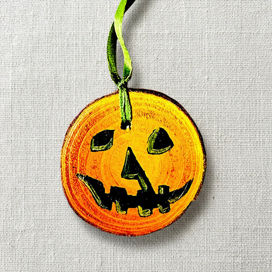 A hand-painted pumpkin decoration made from wood and acrylic, with a green ribbon and an orange face, designed for Halloween decoration.