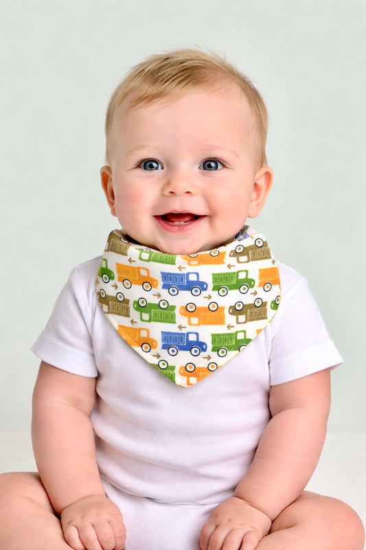 Baby wearing a white shirt with a colorful truck-patterned bib against a plain background