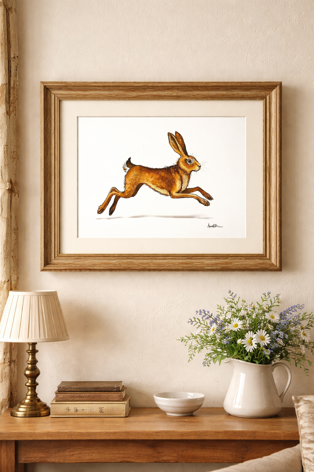 Framed artwork of a leaping hare on a wall above a wooden table with decor items. (Print comes unframed and unmounted)