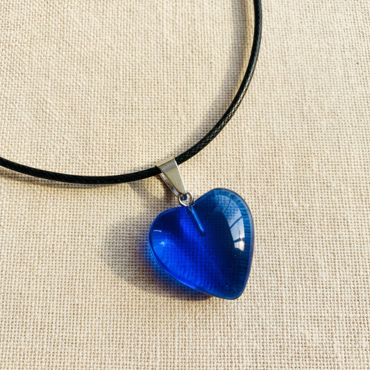 Blue heart-shaped pendant on a black cord against a neutral background