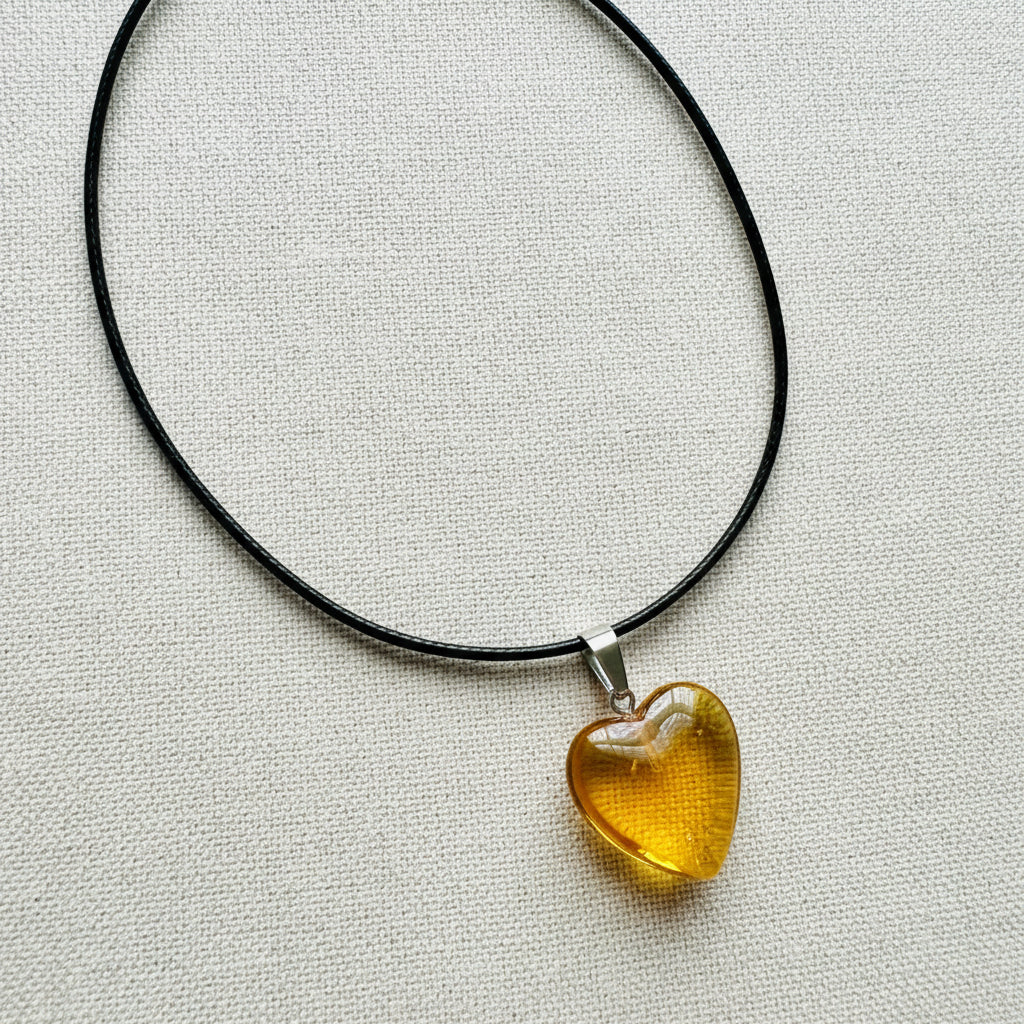 Heart-shaped yellow pendant on a black cord against a neutral background