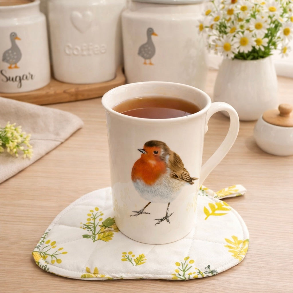 Ceramic mug with a robin design on a floral leaf shaped coaster, surrounded by kitchen items. 