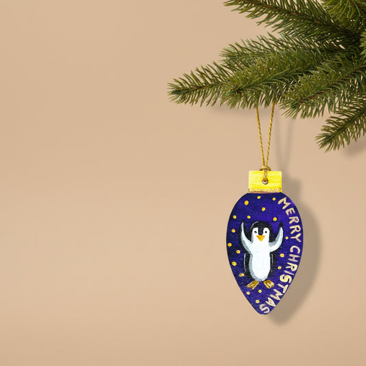 Decorative wooden Christmas ornament with a penguin design on a purple background with merry Christmas text