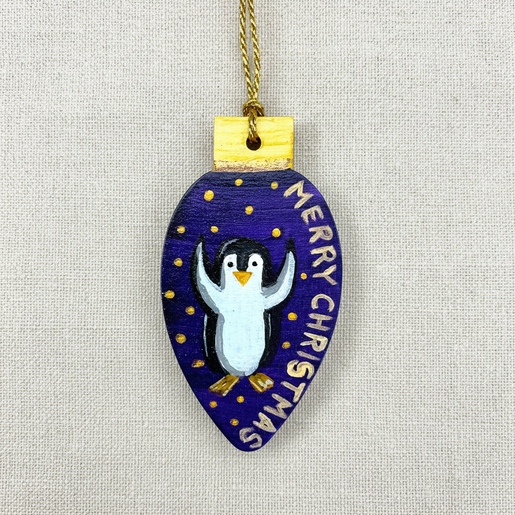 Decorative wooden Christmas tree ornament with a penguin and 'Merry Christmas' text on a blue/purple background.