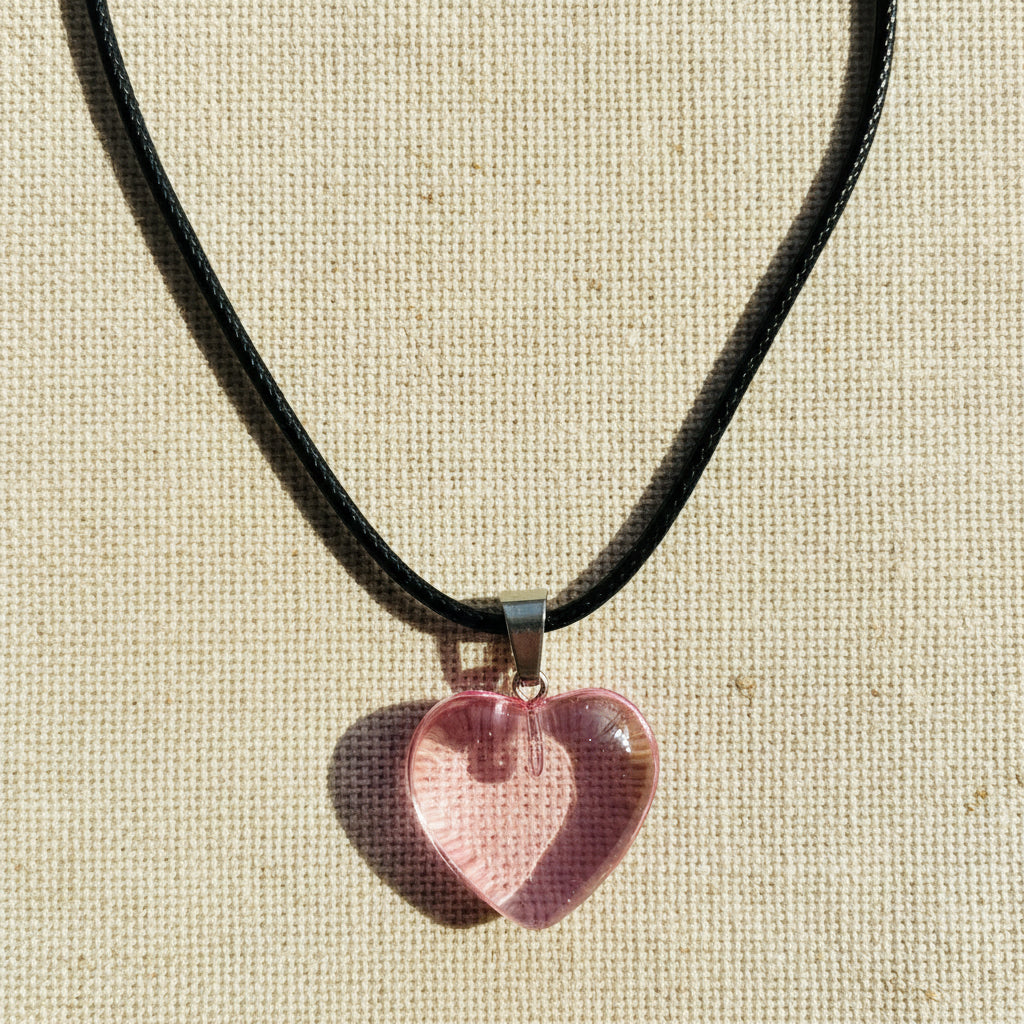 Heart-shaped pink transparent pendant on a black cord against a neutral background