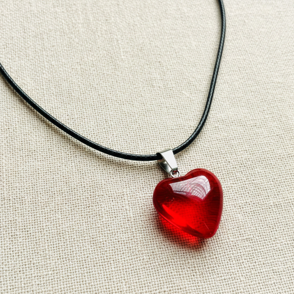 Red heart-shaped pendant on a black cord against a neutral background