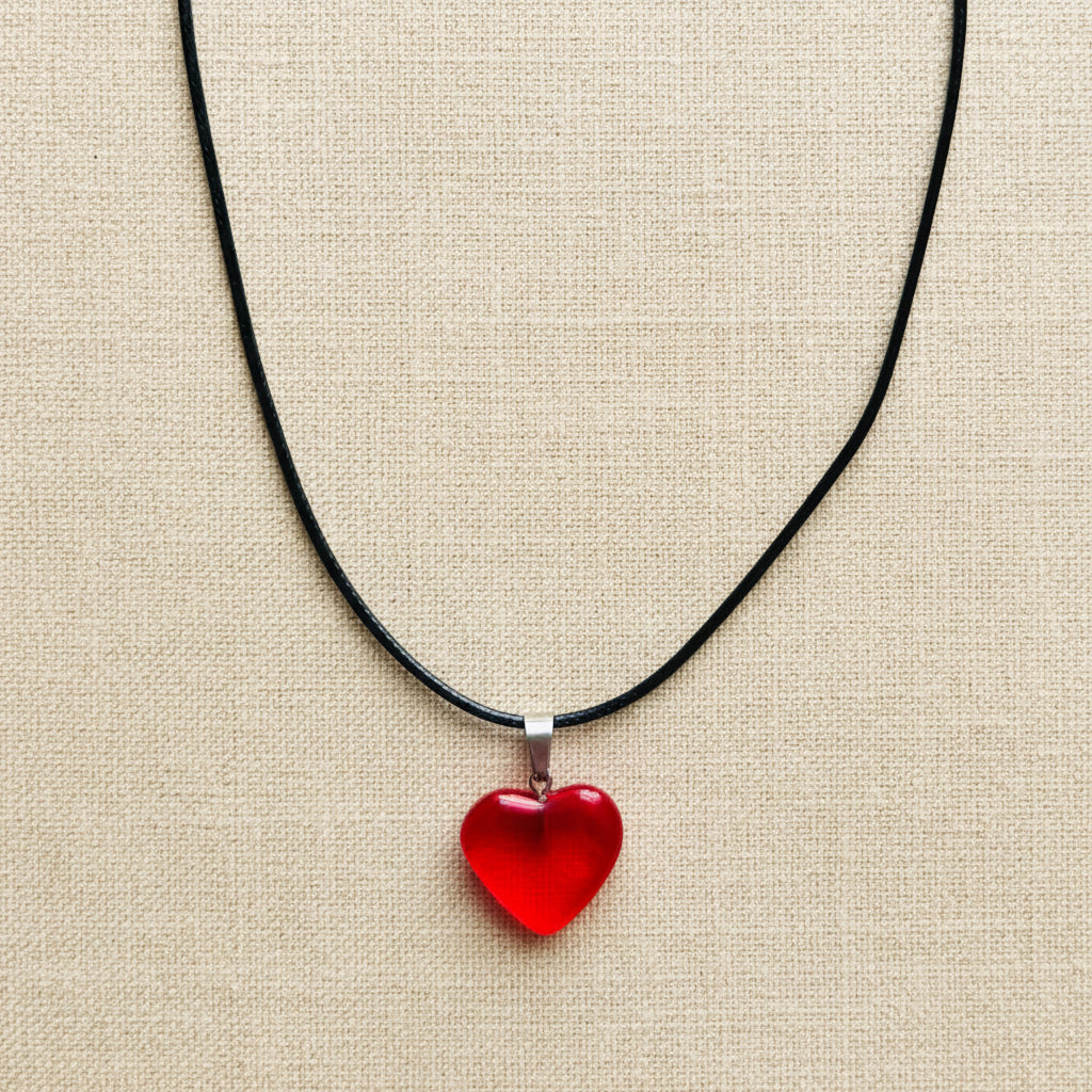Red heart-shaped pendant on a black cord against a neutral background