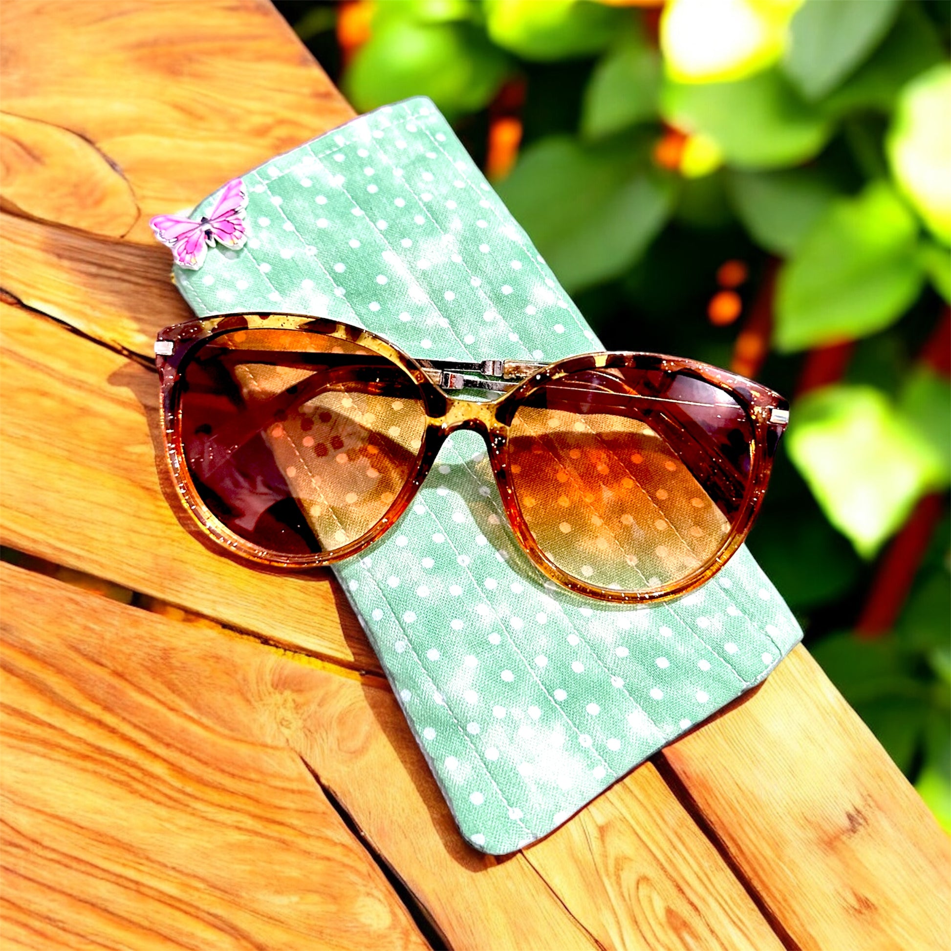 Sunglasses on a green polka dot fabric glasses case with a blurred natural background. Glasses not included.