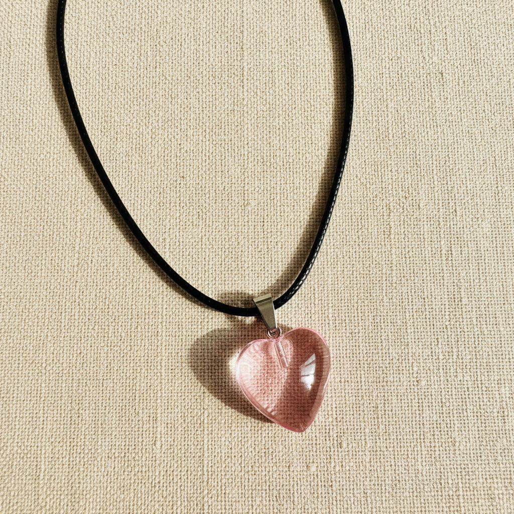 Pink heart-shaped pendant on a black cord against a neutral background