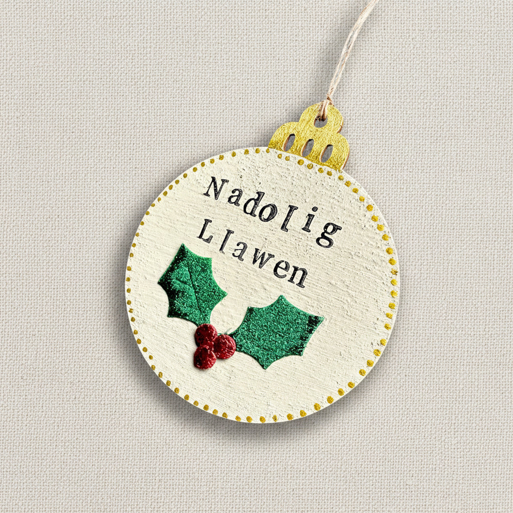 Decorative Christmas tree ornament with 'Nadolig Llawen' text and holly design on a neutral background