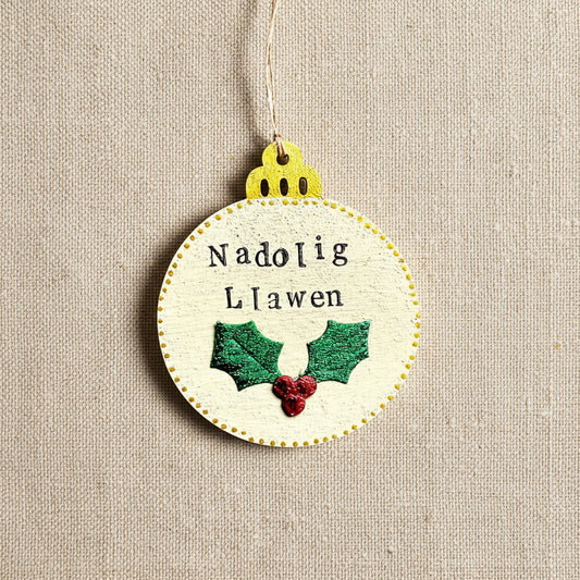 Decorative Christmas ornament with 'Nadolig Llawen' text and holly design.