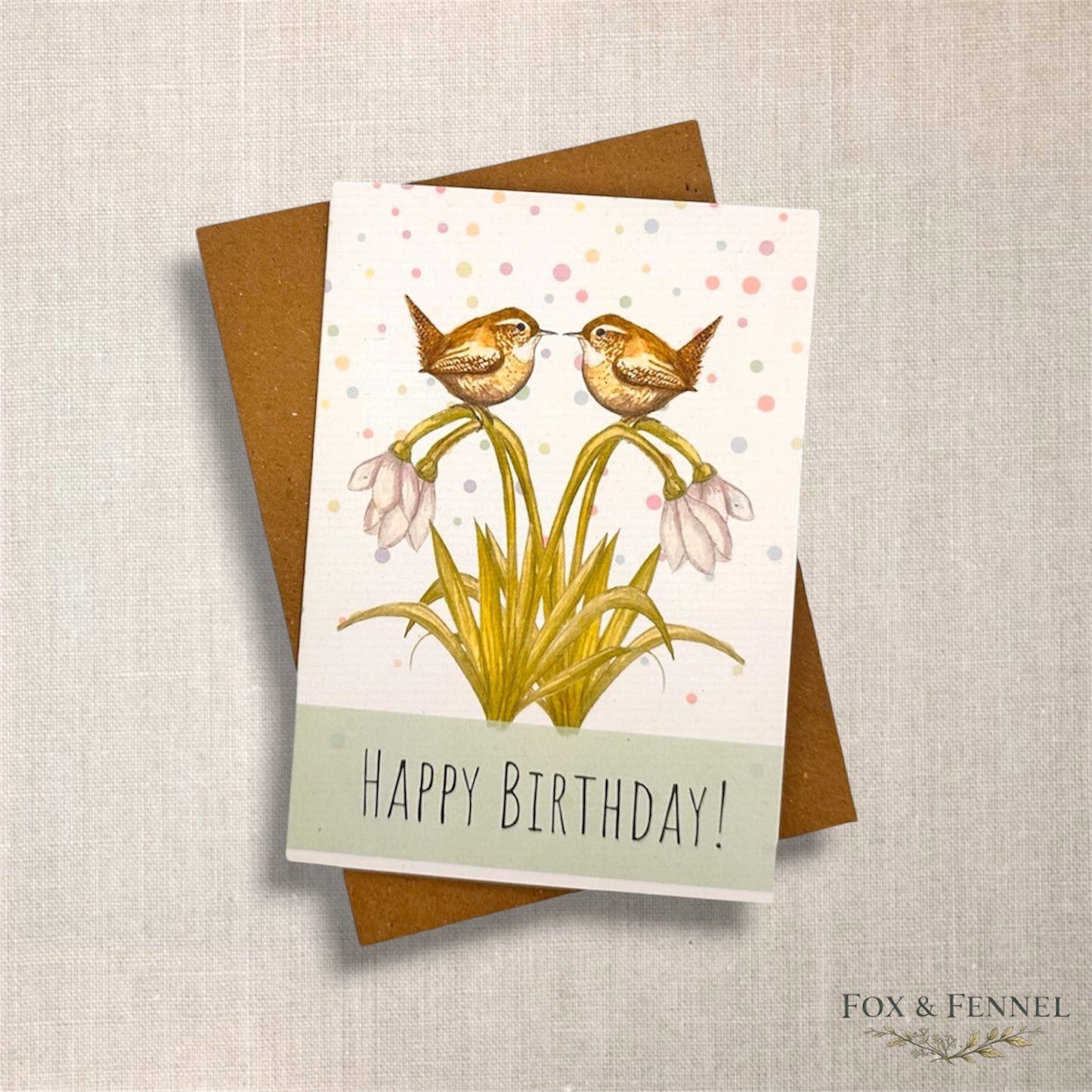 Birthday card with two British wren birds sat on snowdrop flowers and 'Happy Birthday!' text, brown Kraft envelope 