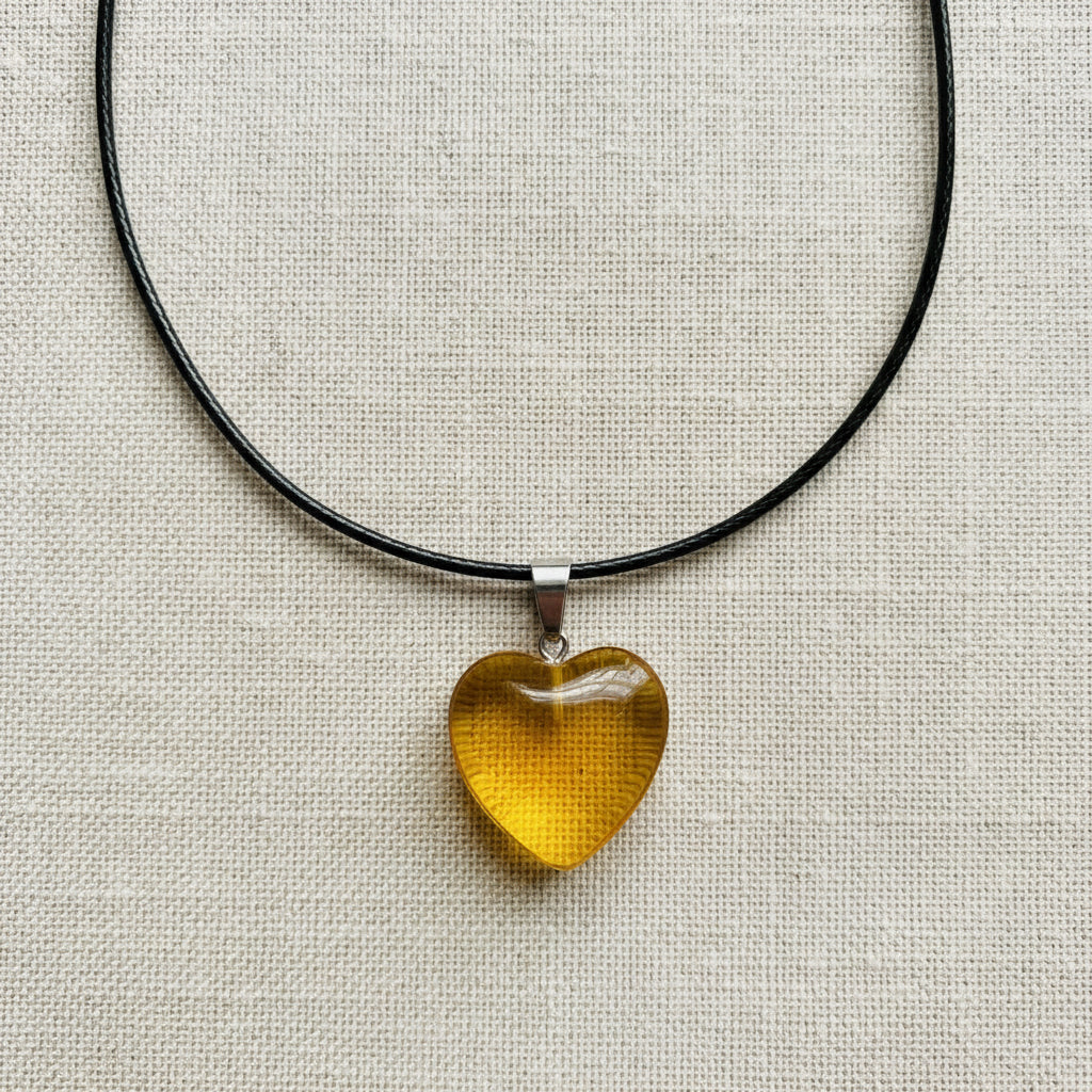 Heart-shaped yellow pendant on a black cord against a neutral background
