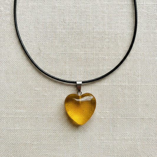 Heart-shaped yellow pendant on a black cord against a neutral background