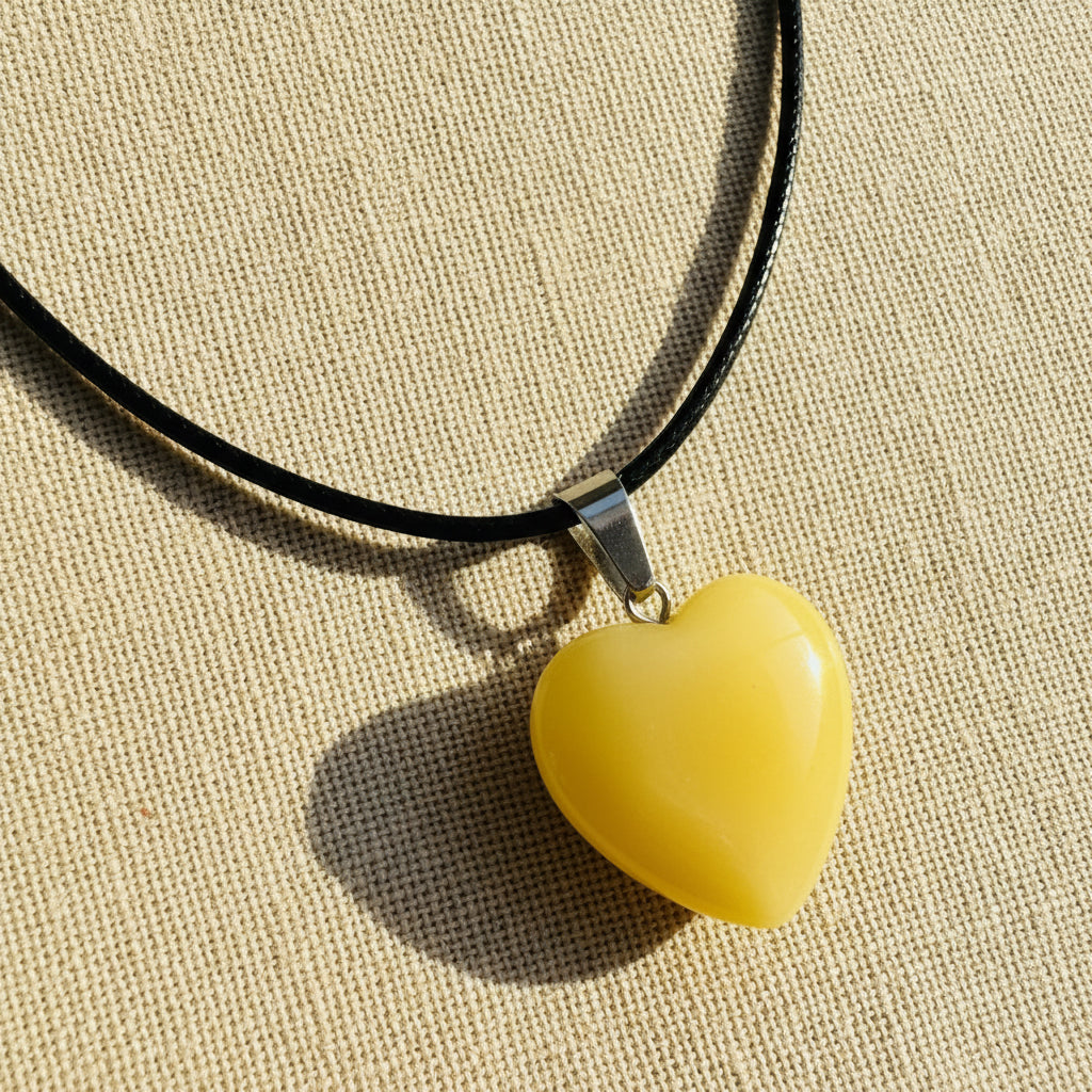 Yellow heart-shaped pendant on a black cord against a neutral background