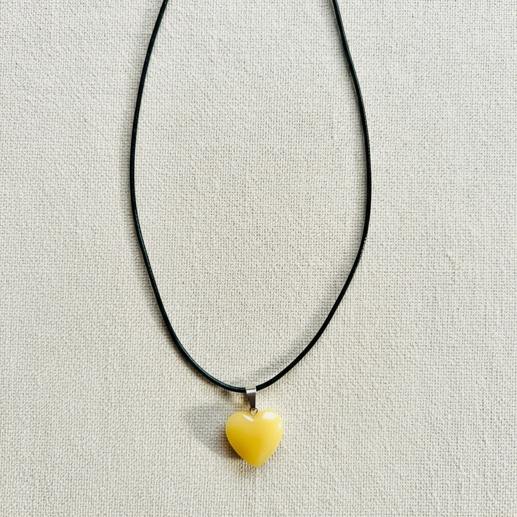 Yellow heart-shaped pendant on a black cord against a neutral background