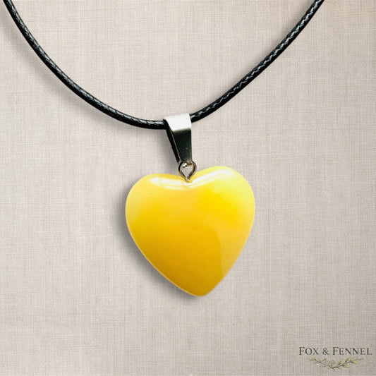 Yellow heart-shaped pendant on a black cord against a beige background