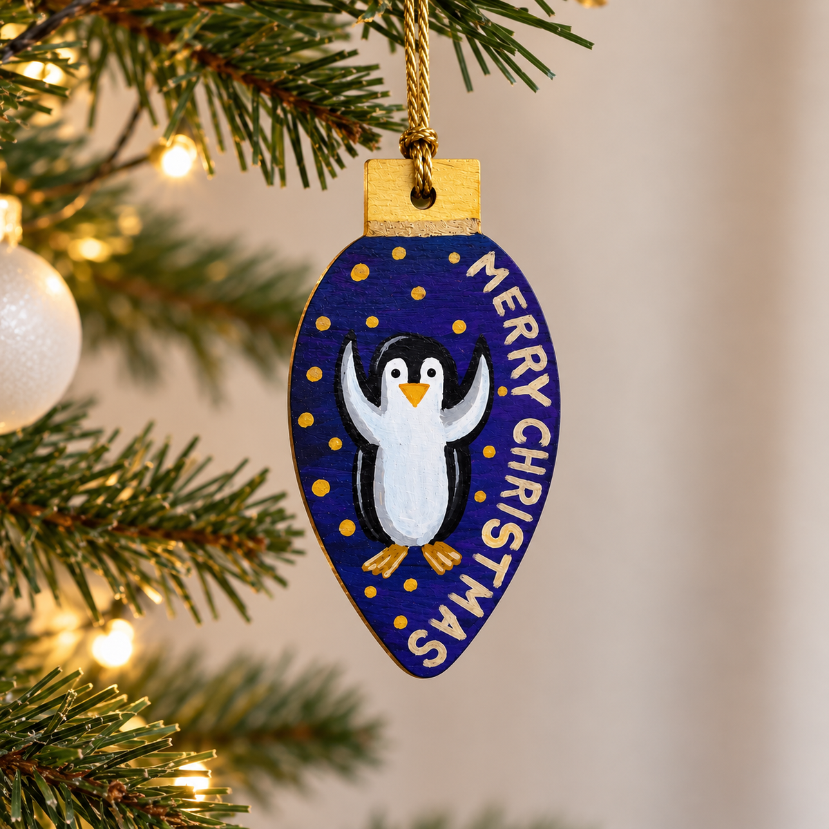 Hand-painted wooden penguin Christmas ornament hanging from a Christmas tree with warm fairy lights